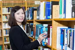 A student is in the library and smiling to the camera