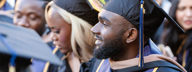 A SFBU graduate sits at commencement ceremony in their full regalia, in the midst of other SFBU graduates