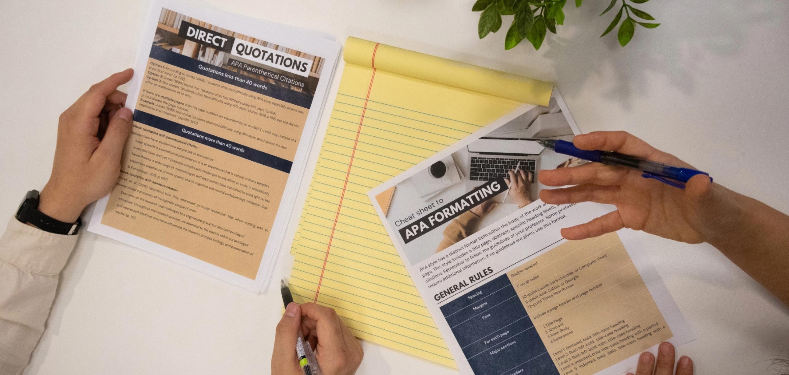 APA formatting cheat sheet with a notepad on a desk with four hands hovering over them.