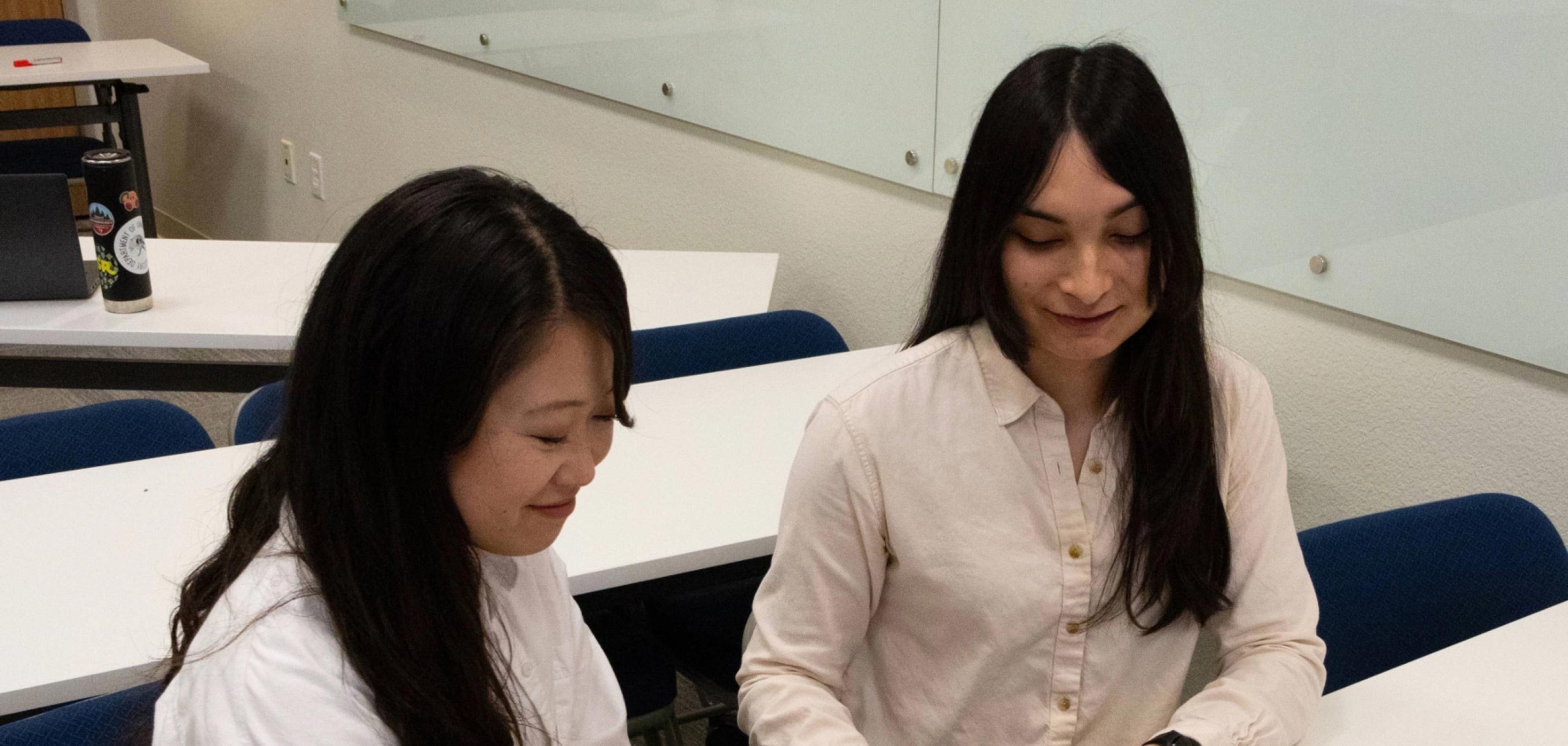 Two smiling Student Support Specialists are talking in the classroom
