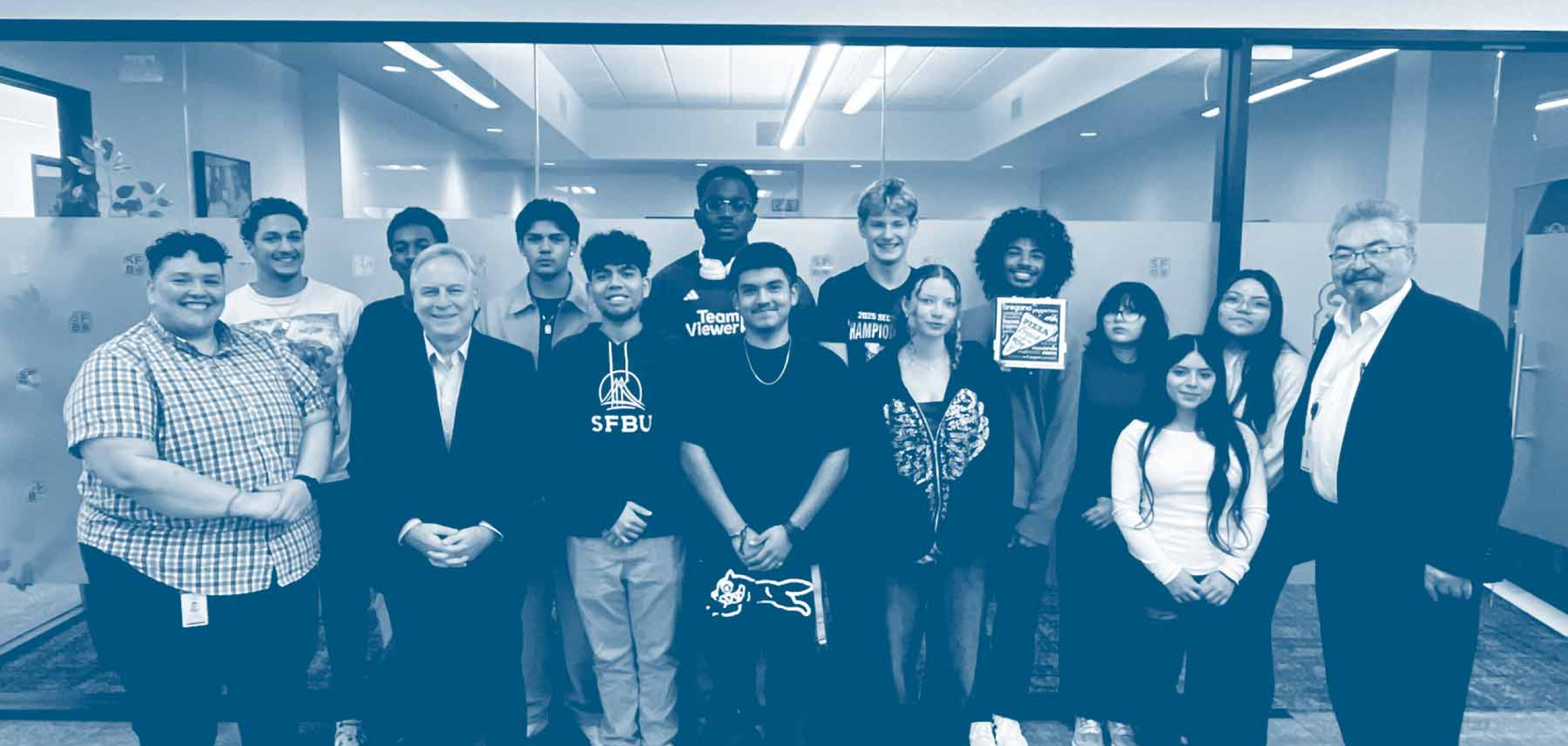 Group of students and faculty stand together in a hallway, posing for a group photo inside a campus building.