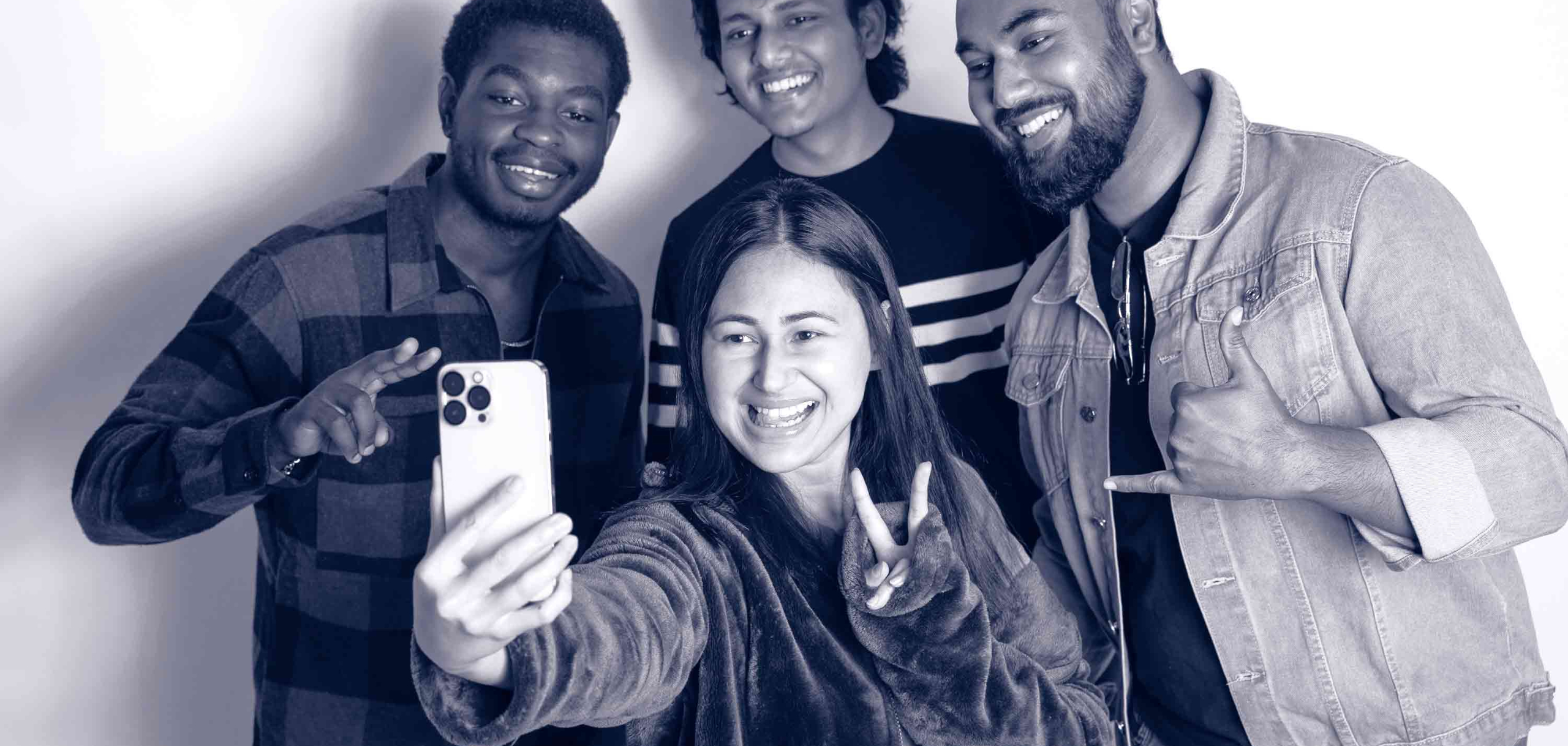 Group of students smile and take a selfie together, posing with hand gestures against a plain background.