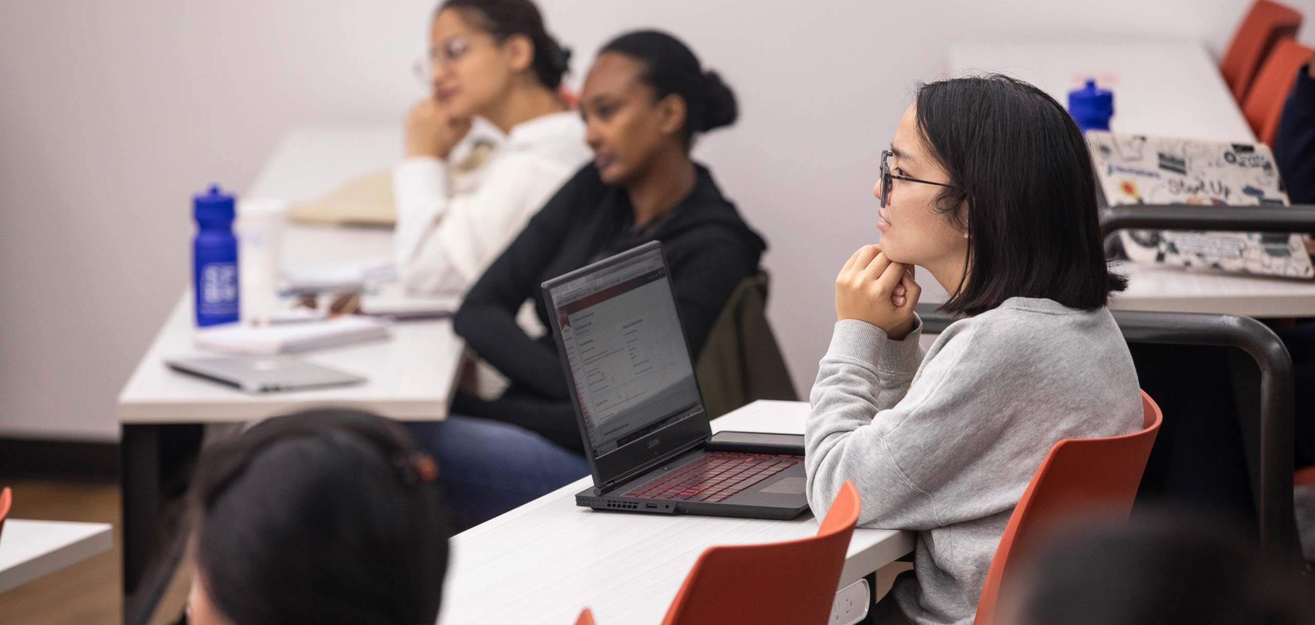 Three students in a classroom sitting at a their desk listening to a lecture.
