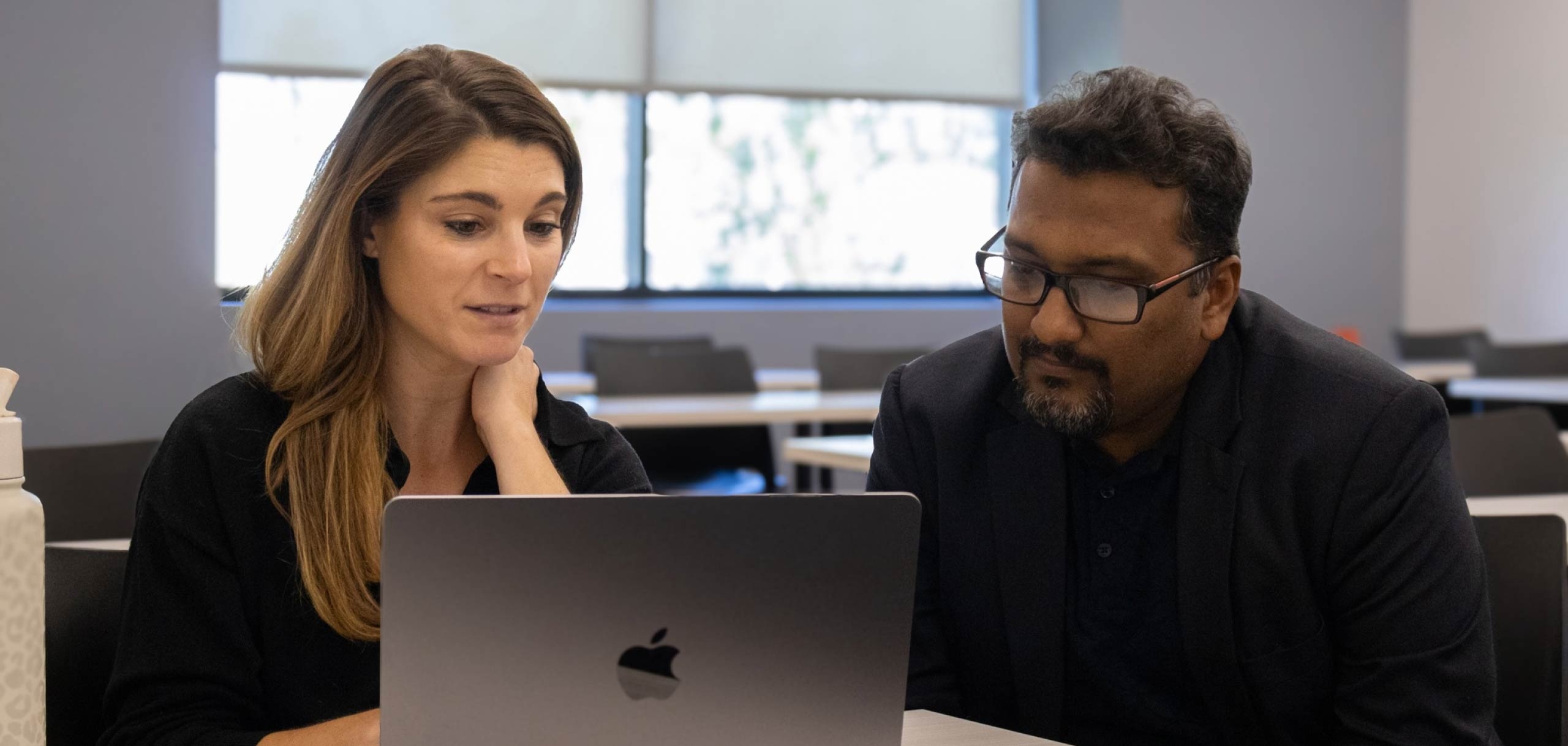 Two faculty members talking infront of a laptop.