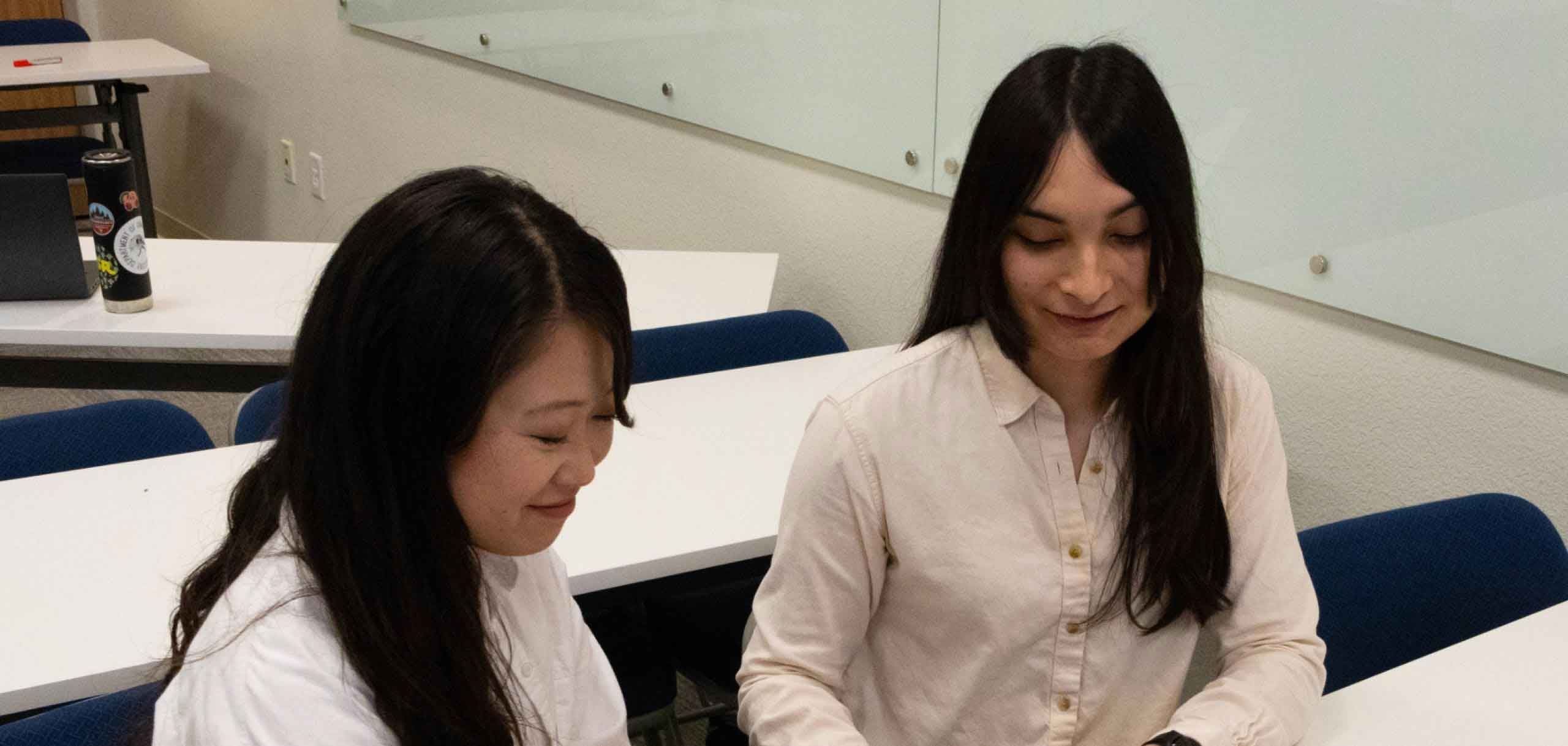 Two smiling Student Support Specialists are talking in the classroom