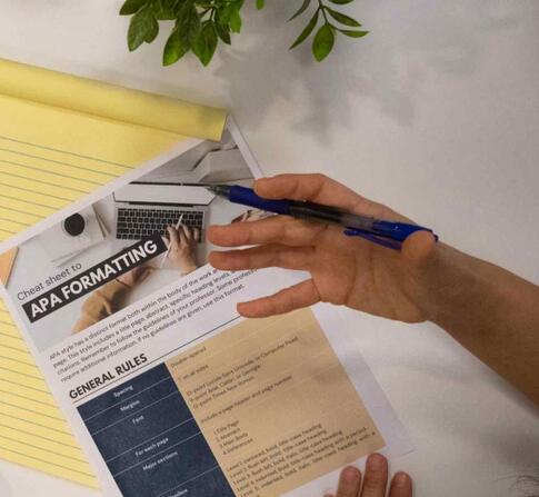 APA formatting cheat sheet with a notepad on a desk with four hands hovering over them.