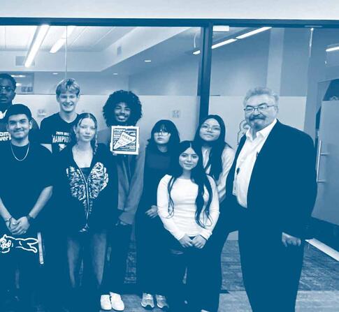 Group of students and faculty stand together in a hallway, posing for a group photo inside a campus building.