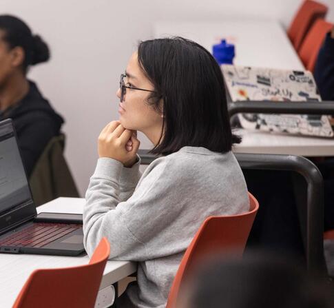 Three students in a classroom sitting at a their desk listening to a lecture.