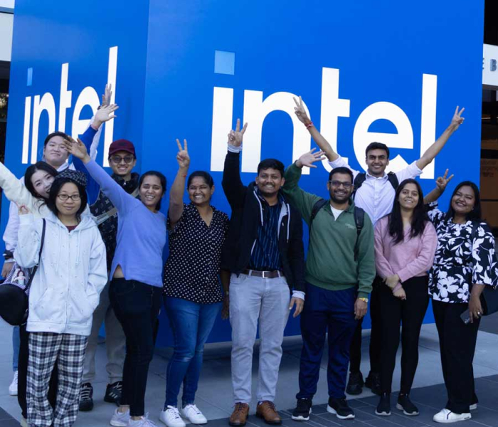 Happy students smiling towards the camera in front of an intel sign
