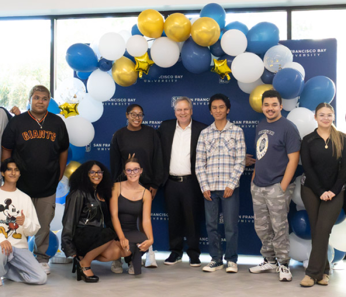 Student under a celabratory prop with balloons smiling