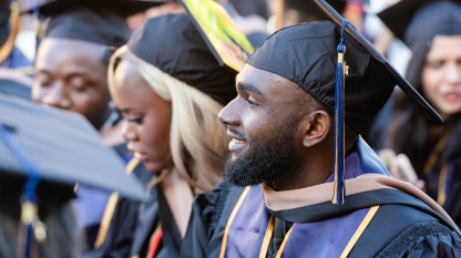 A SFBU graduate sits at commencement ceremony in their full regalia, in the midst of other SFBU graduates