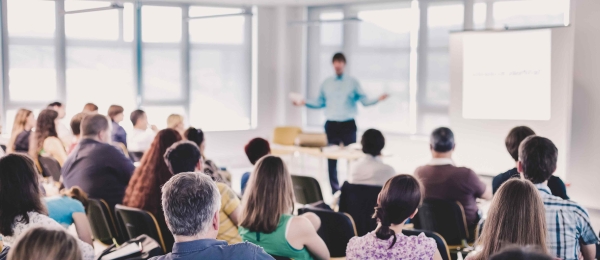 Speaker giving a presentation to a crowd of people sitting on chairs.